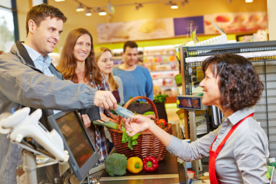 Smiling man paying groceries at supermarket checkout with Euro money bill