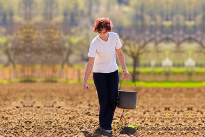 Young woman farmer planting seeds mixed with fertilizer from a bucket